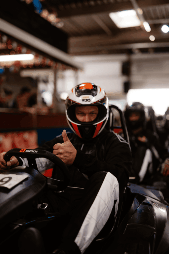 Ein Fahrer mit dunkelblauem Overall hebt im Kartcenter Cologne vor dem Start beim Kartfahren Köln den Daumen.